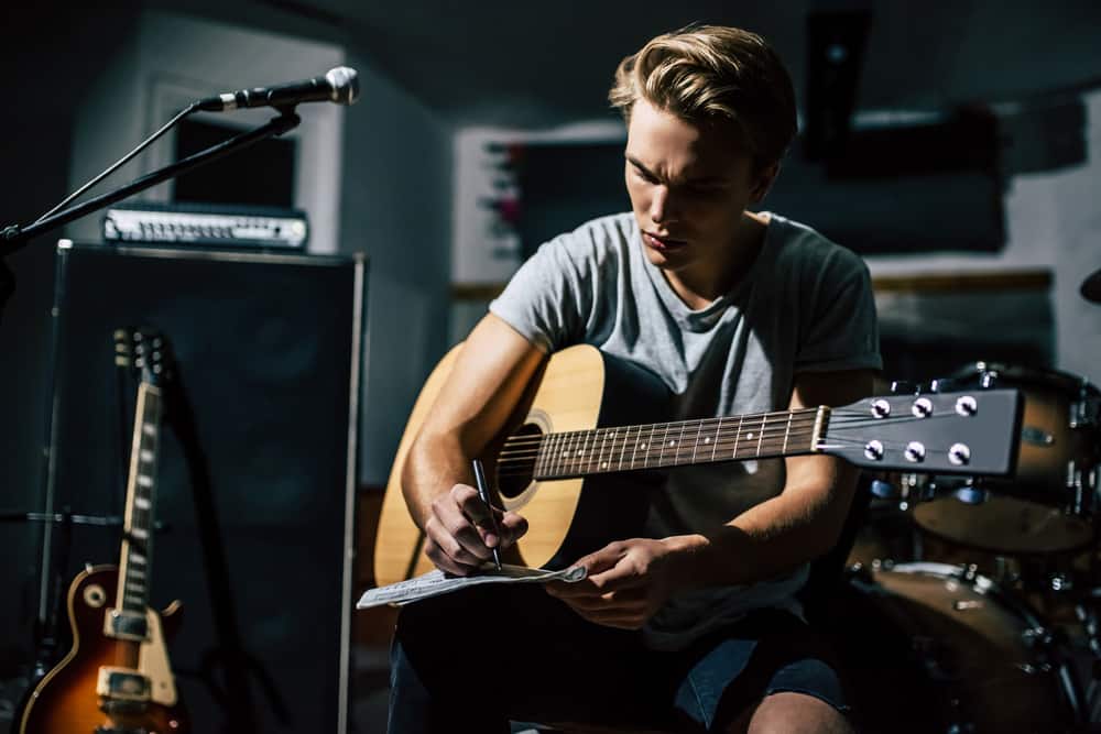 Songwriter with acoustic guitar writing lyrics in notebook