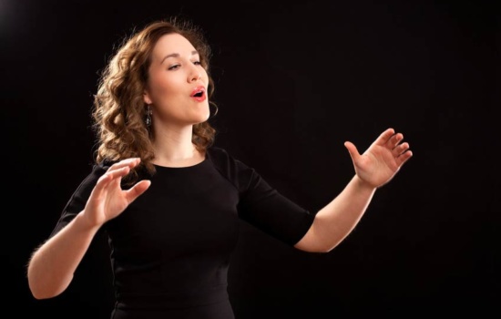 Female Choir Director conducting choir against dark background