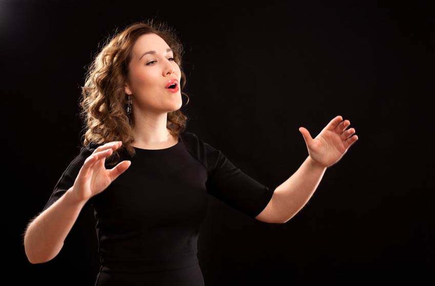 Female Choir Director conducting choir against dark background