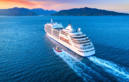 Cruise ship with smaller boat on the ocean near mountains