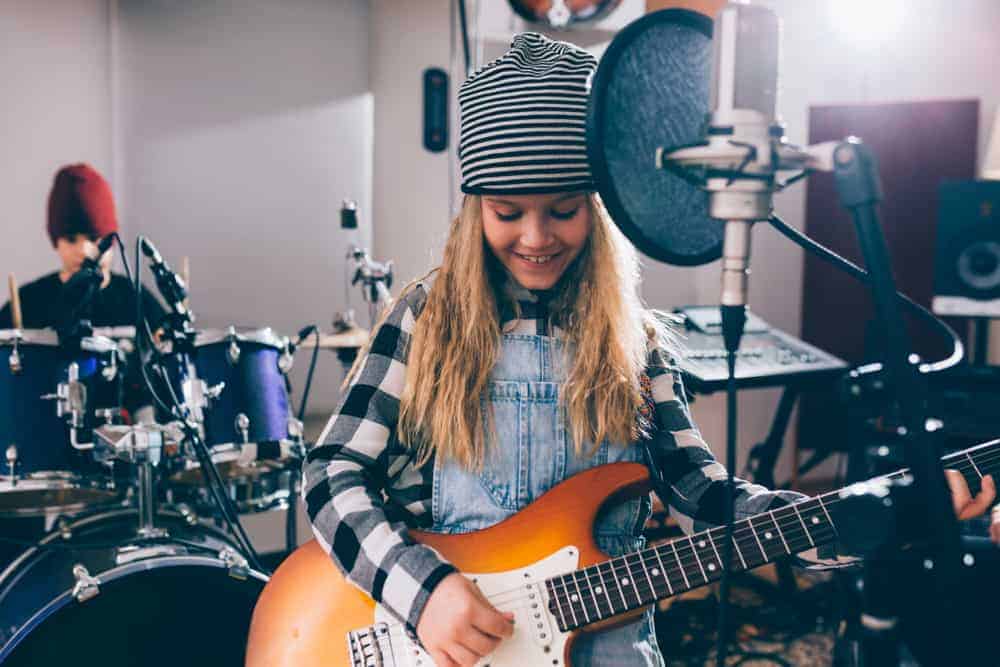 Young girl playing guitar in studio with young boy on drums