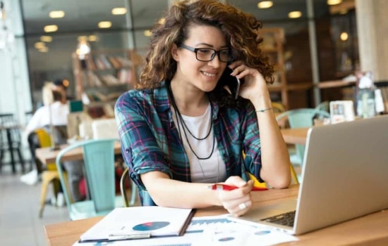 Female director of development on cell phone looking at laptop in open plan office