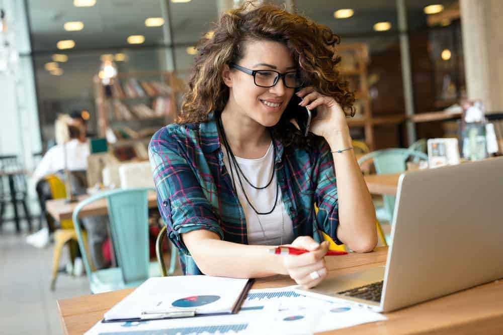 Female director of development on cell phone looking at laptop in open plan office