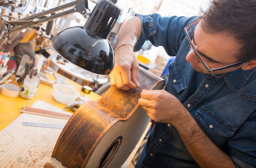 Instrument repair and restoration specialist fixing a guitar in his workshop