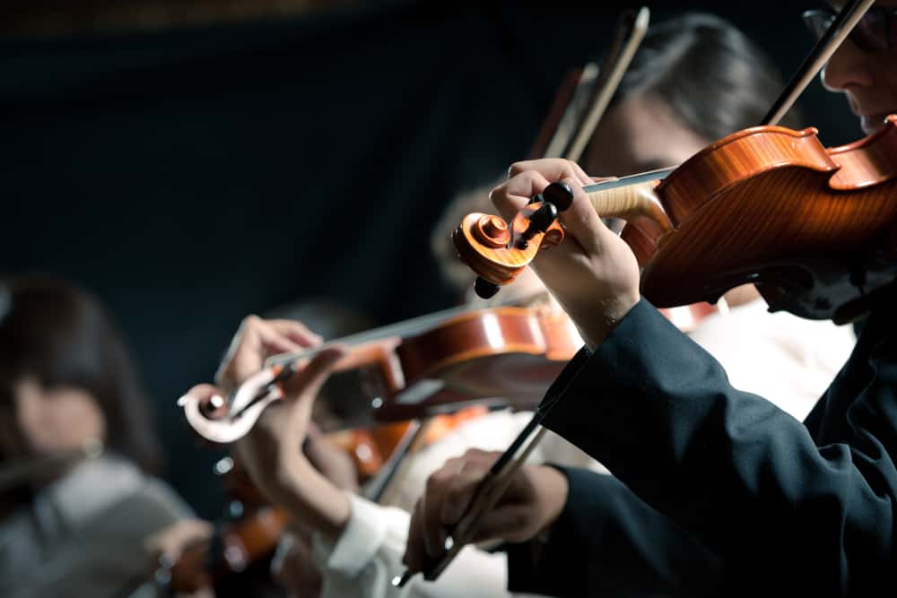 Symphony orchestra violinists performing on stage against dark background