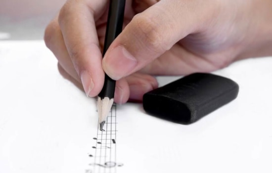 Closeup on an Orchestrator's hand writing notes on sheet music