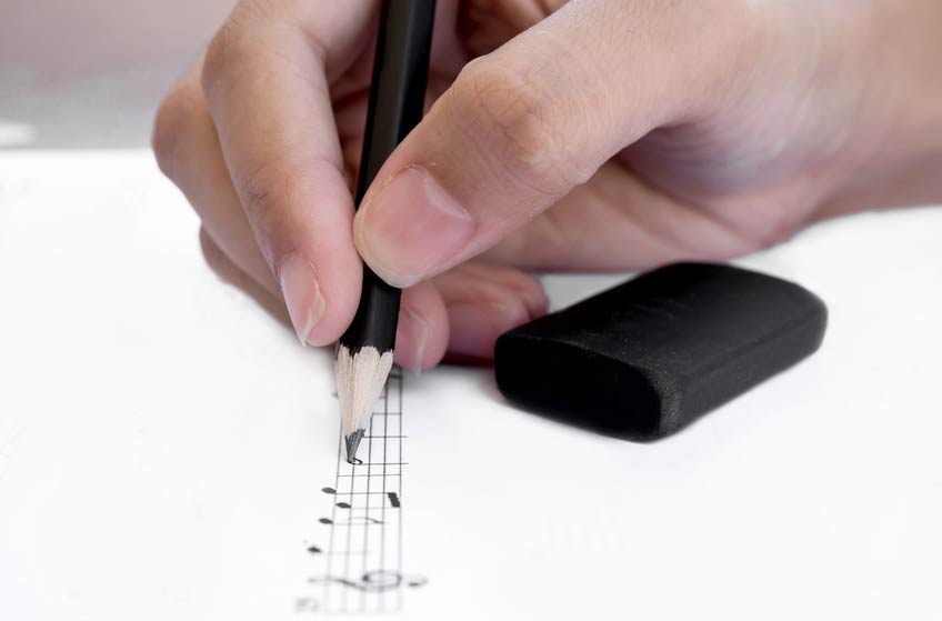 Closeup on an Orchestrator's hand writing notes on sheet music