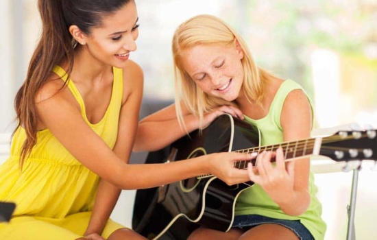 Private Instrument Teacher showing young female student how to play guitar