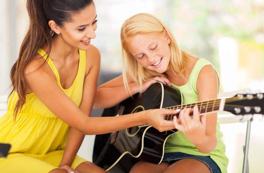 Private Instrument Teacher showing young female student how to play guitar