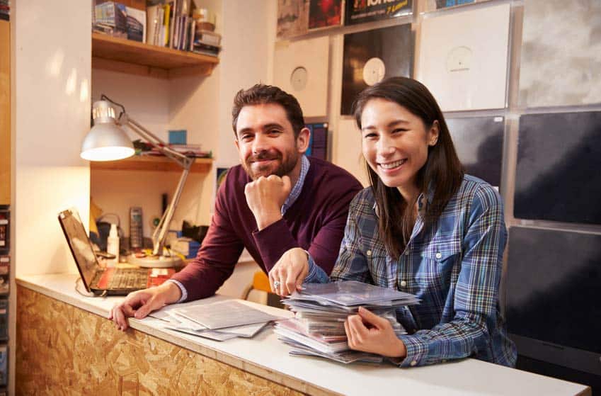 Two record label employees with vinyl releases on the wall behind them