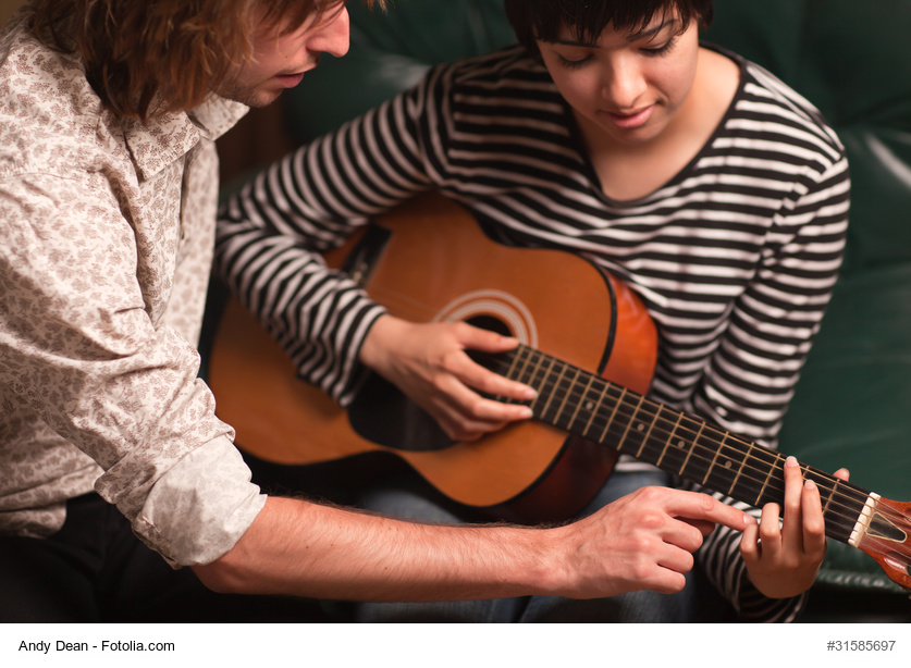 Young Male Musician Teaches Female Student How To Play the Guitar.