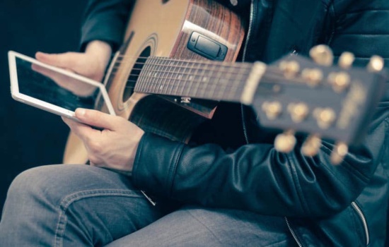 Musician using tablet and holding his acoustic guitar
