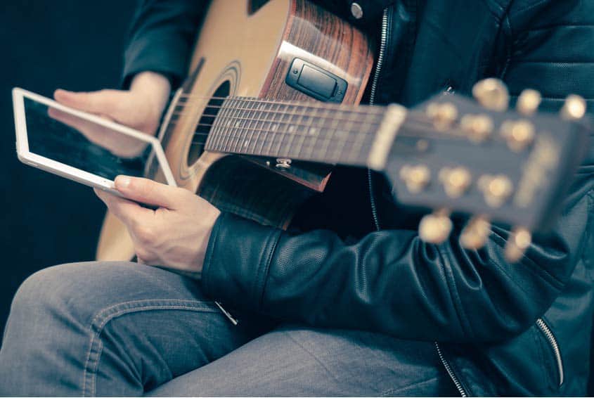 Musician using tablet and holding his acoustic guitar