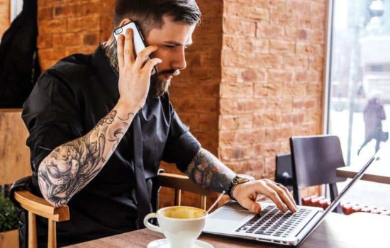 Business Manager looking at his laptop and talking on the phone in a cafe