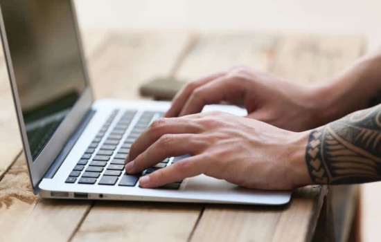 Close up image of tattooed hands using computer