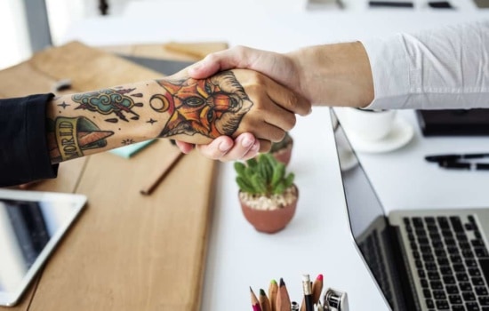 Tattooed artist shaking hands with person in dress shirt