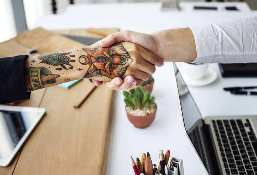 Tattooed artist shaking hands with person in dress shirt