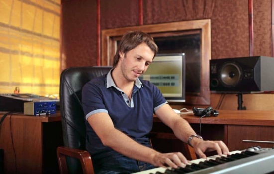 Video Game Composer writing music on his keyboard in a recording studio