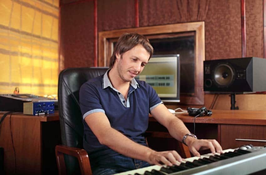 Video Game Composer writing music on his keyboard in a recording studio