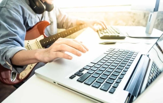 Guitar player with instrument and headphones on laptop