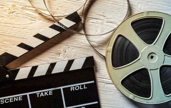 Film clapperboard and roll of film on wooden background