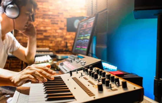 Asian male film music composer playing midi keyboard synthesizer in sound studio