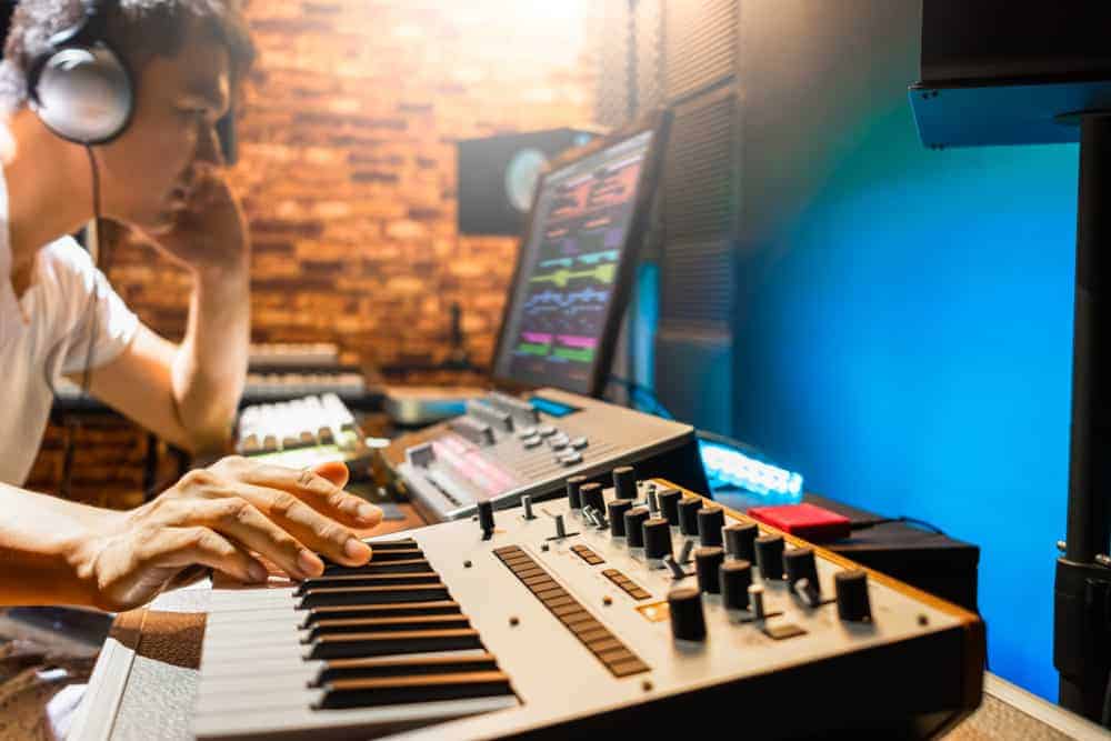 Asian male film music composer playing midi keyboard synthesizer in sound studio