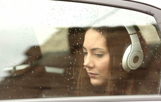 Girl with headphones looking wistfully out the car window