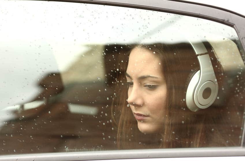 Girl with headphones looking wistfully out the car window