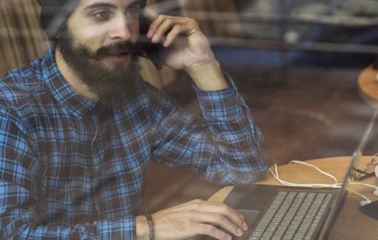 Young bearded man talking on his cellphone while on his laptop
