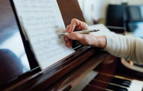 Copyist writing sheet music while leaning on piano