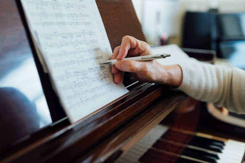 Copyist writing sheet music while leaning on piano