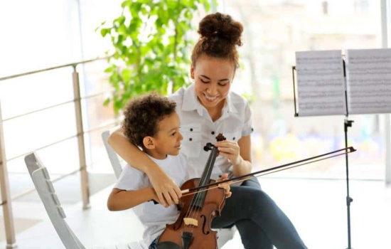 Young female music instructor teaching little boy how to play the violin