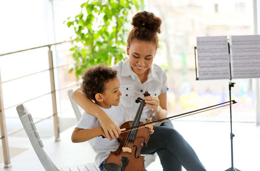 Young female music instructor teaching little boy how to play the violin