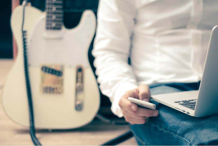 Guitar player checking social media on his phone and his laptop