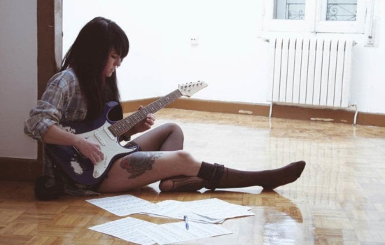 Female songwriter writing music on her guitar with sheet music on the floor