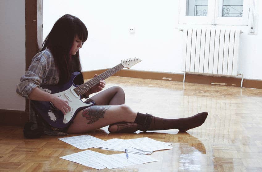 Female songwriter writing music on her guitar with sheet music on the floor