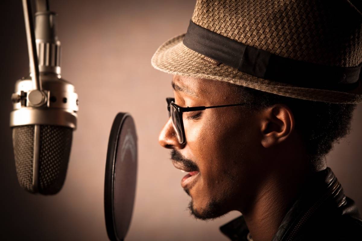 Stylish black man with hat singing into microphone with pop filter