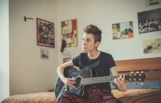 Young non-binary musician playing guitar in their bedroom