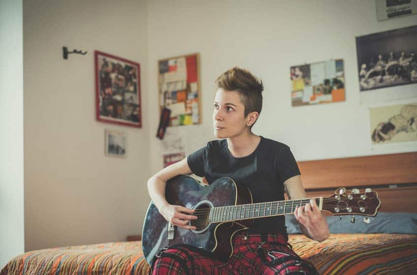 Young non-binary musician playing guitar in their bedroom