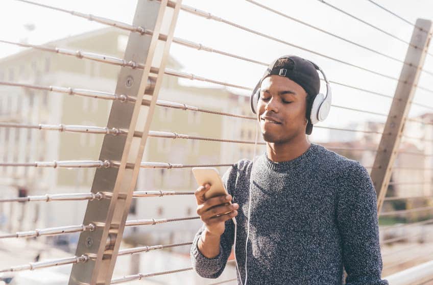 Young black man listening to music on his smart phone via headphones
