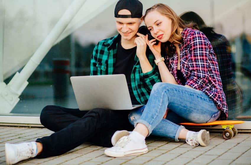 Two young musicians listening to headphones and checking out laptop outdoors