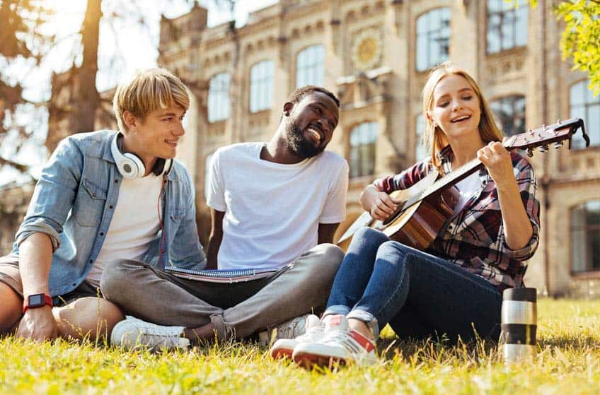 Music students playing guitar on the grounds of college campus