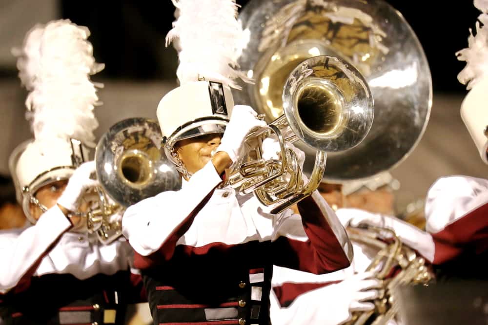 Marching band in white and maroon uniforms playing brass instruments