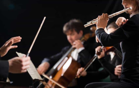 Flute player, violinist, and cellist performing in orchestra with conductor