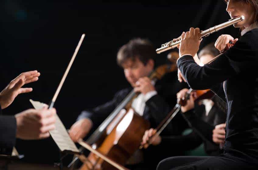 Flute player, violinist, and cellist performing in orchestra with conductor