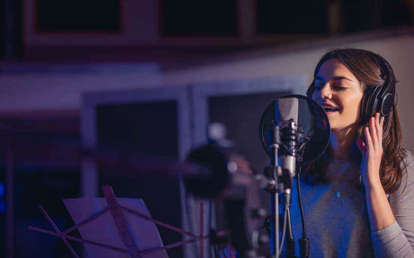 Female vocalist singing into microphone and pop filter in recording studio