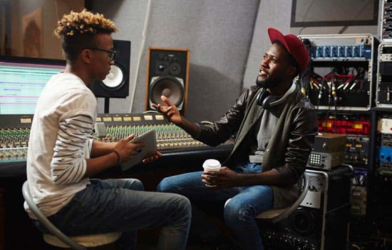 Two young black male music producers talking in recording studio