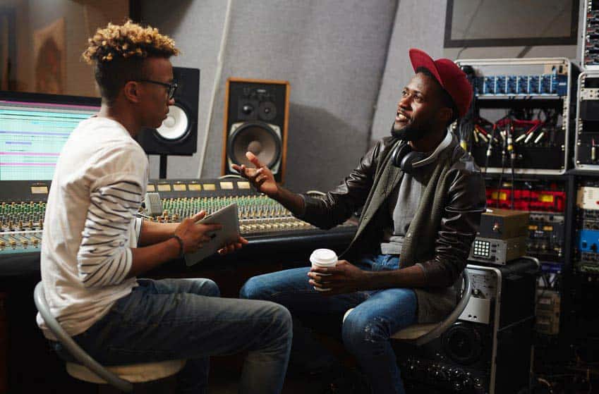 Two young black male music producers talking in recording studio