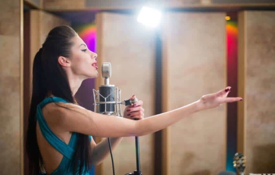 Young woman singing into microphone in recording studio